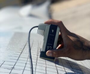 A close-up of a technician's hand using a specialized device to inspect wind turbine blade surface for defects.