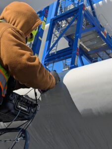 Technician inspecting wind turbine blades during cold weather using advanced tools.